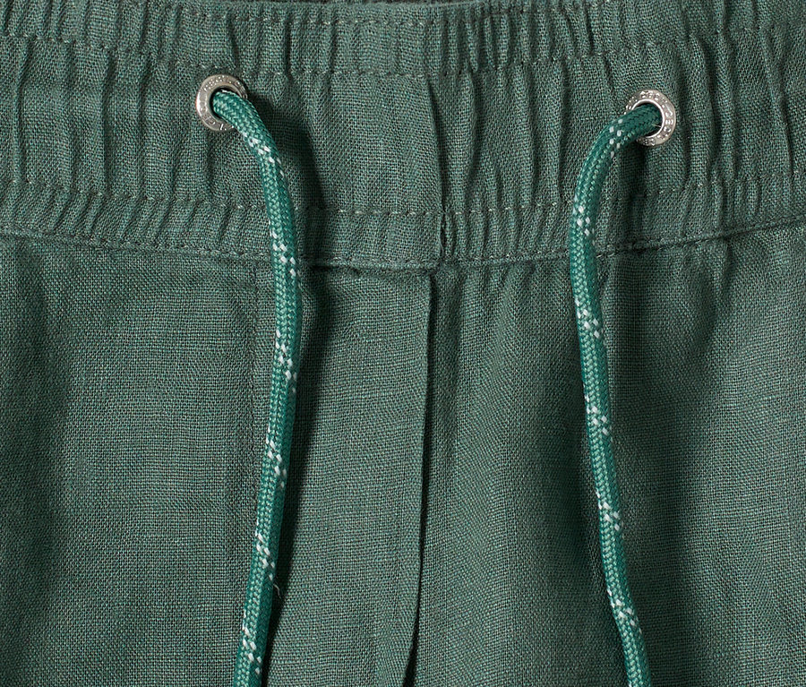 Gros plan d'un pantalon vert avec cordon de serrage et œillets argentés.