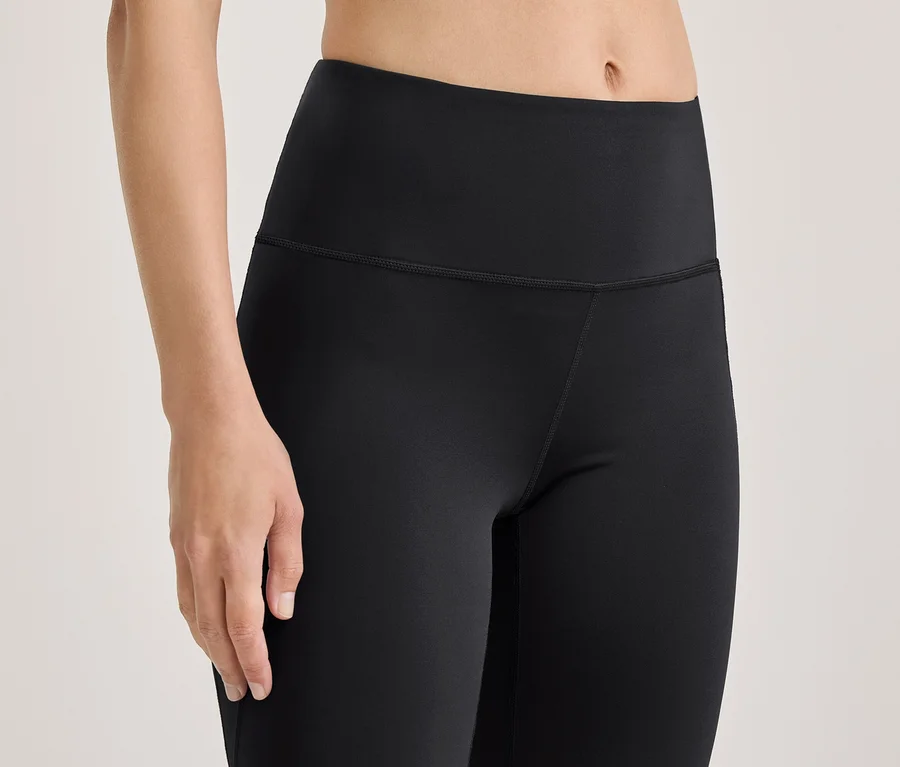 Gros plan d'une personne portant un legging noir taille haute, montrant son torse, le haut de ses jambes et son bras gauche.