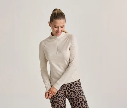 Femme souriante avec une queue de cheval, portant un haut côtelé clair à manches longues avec un zip court et un legging léopard.