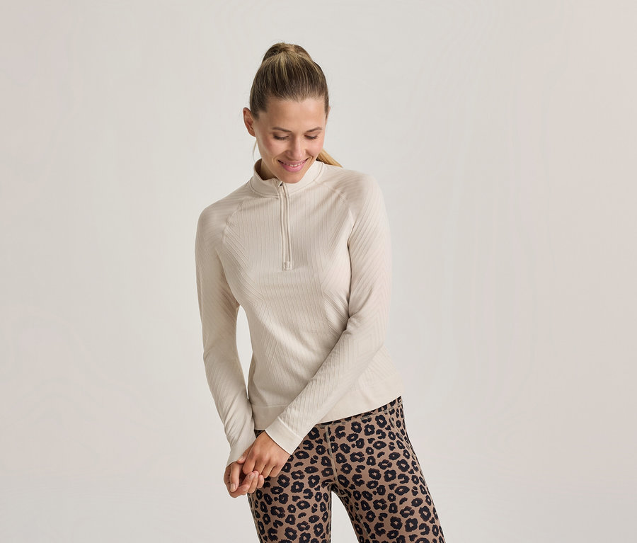 Femme souriante avec une queue de cheval, portant un haut côtelé clair à manches longues avec un zip court et un legging léopard.