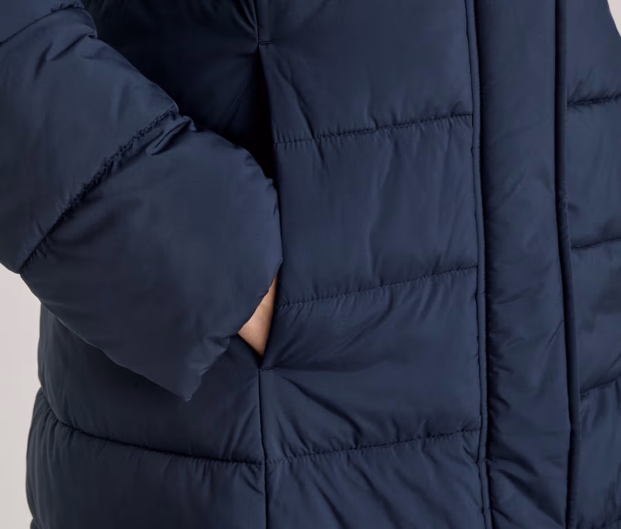 Main glissée dans la poche latérale d'une doudoune matelassée bleu foncé.
