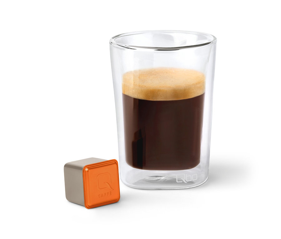 Un verre de Qbo Caffè MINAS VERDE à côté d'une capsule.