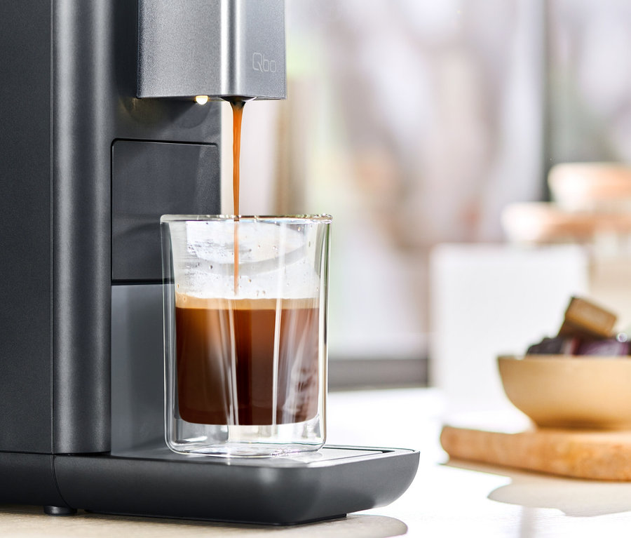 Le café coule d'une machine à café Qbo ESSENTIAL Dark Stone dans un verre.