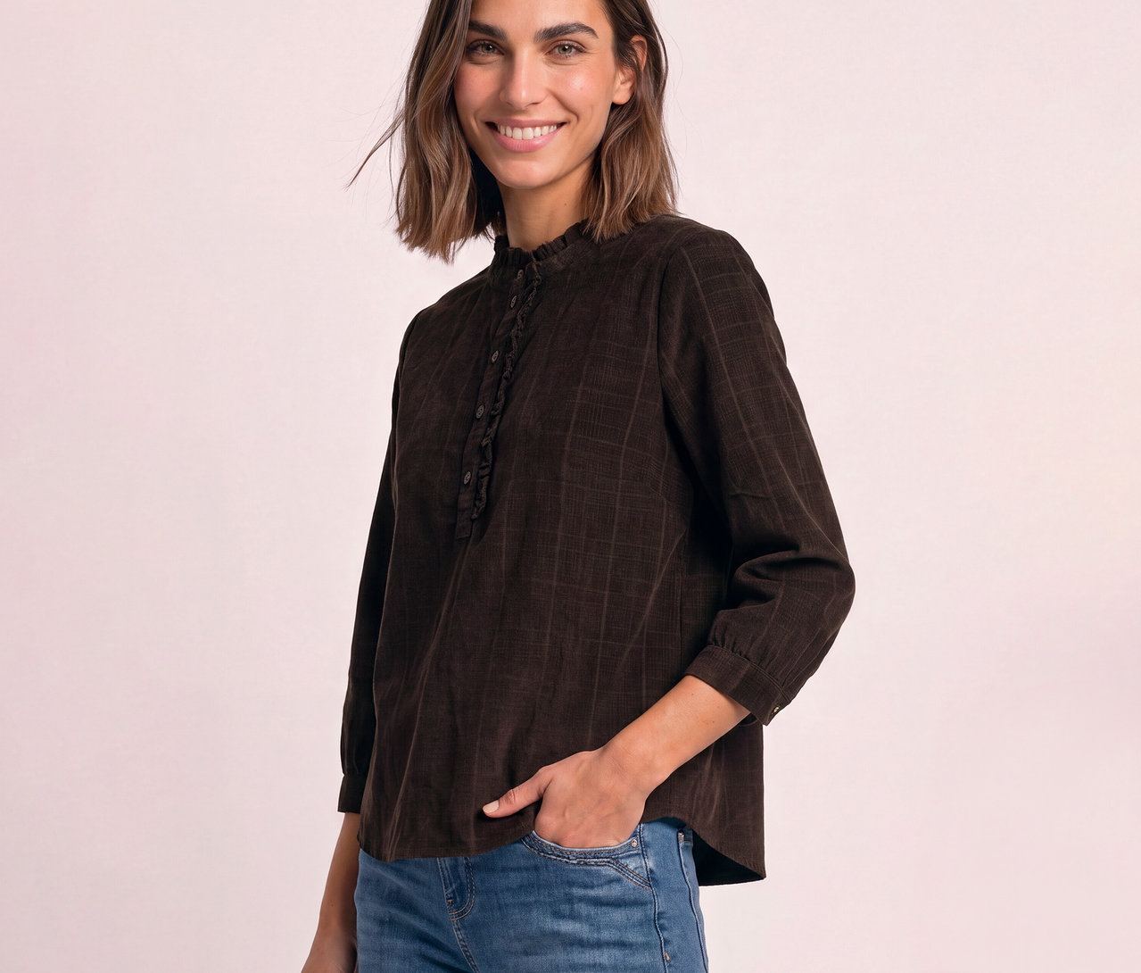Femme souriante portant un chemisier en velours côtelé Street One marron avec col montant à volants, la main gauche dans la poche.