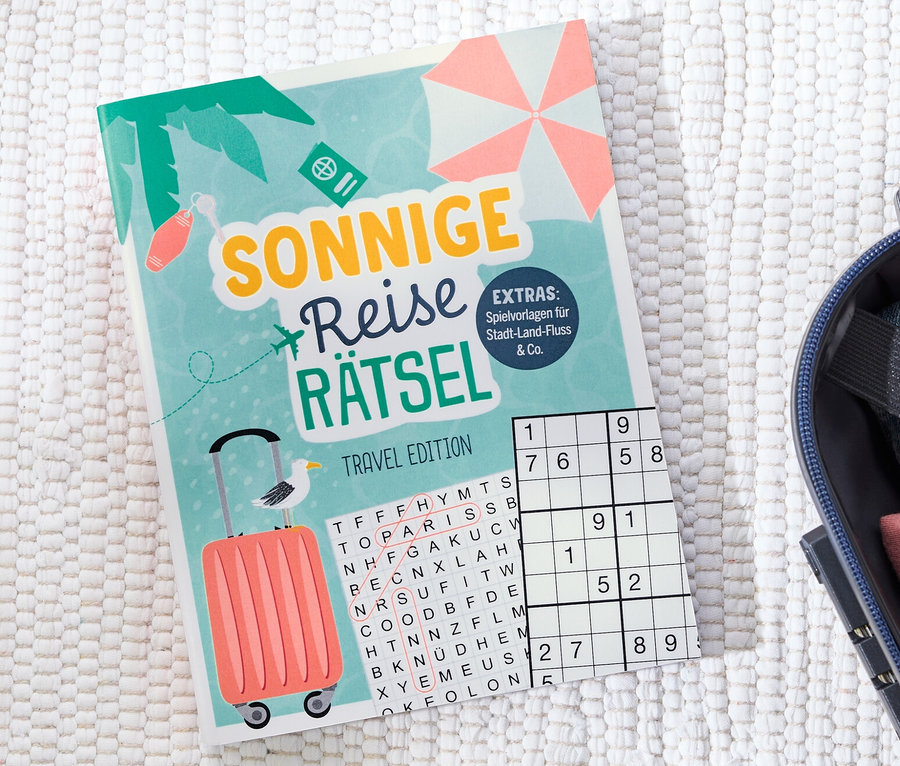 Le livre « Sonnige Reise Rätsel » est posé à côté d'une valise ouverte.