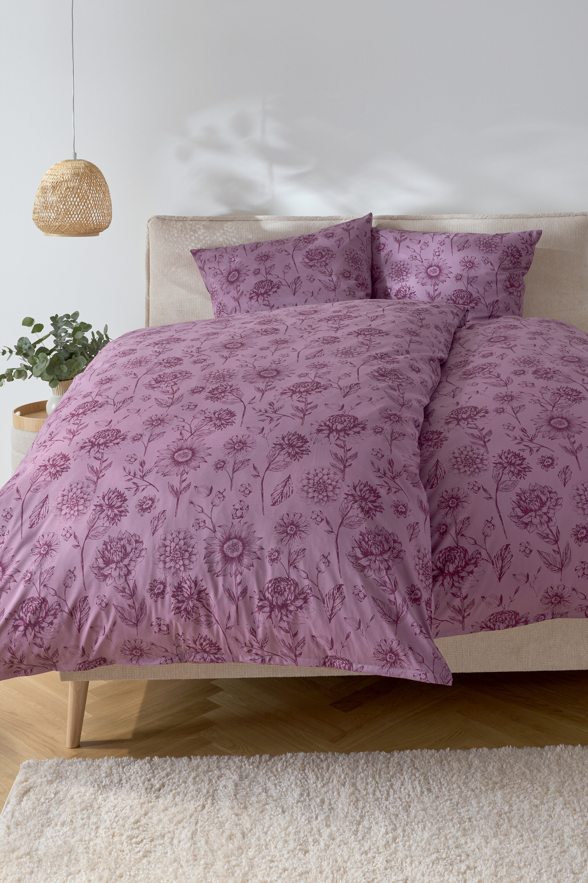 Chambre avec un lit avec des draps à fleurs violets et deux oreillers.