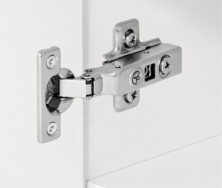 Détail d'une charnière argentée sur une armoire blanche.