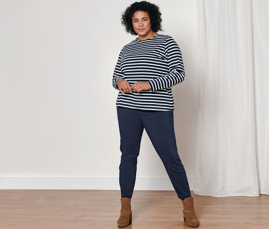 Femme posant en T-shirt manches longues à rayures bleues, pantalon stretch bleu foncé et bottines en cuir velours.
