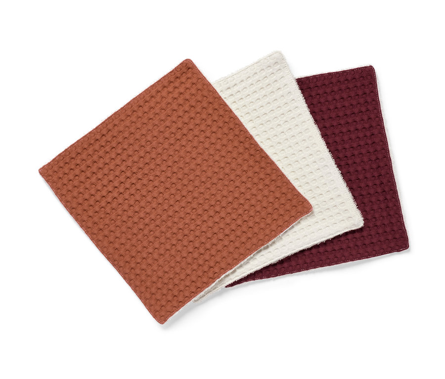Gros plan sur trois lavettes absorbantes en marron, crème et bordeaux.