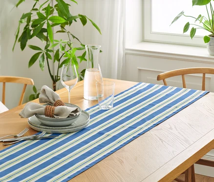 Table dressée avec un chemin de table en coton rayé, des assiettes, des verres et des serviettes en lin.