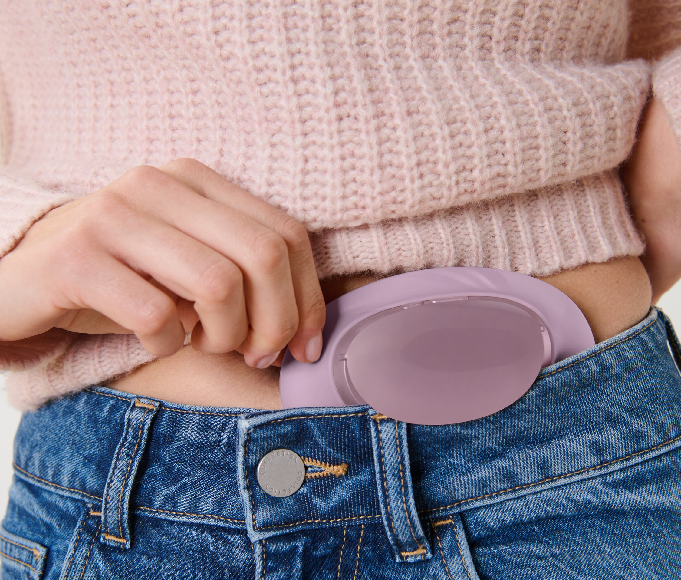 Femme plaçant un chauffe-ventre sans fil dans la poche d'un jean.