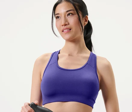 Femme tenant une bouteille d'eau noire et portant une brassière de sport violette (2
paires de brassières de sport).