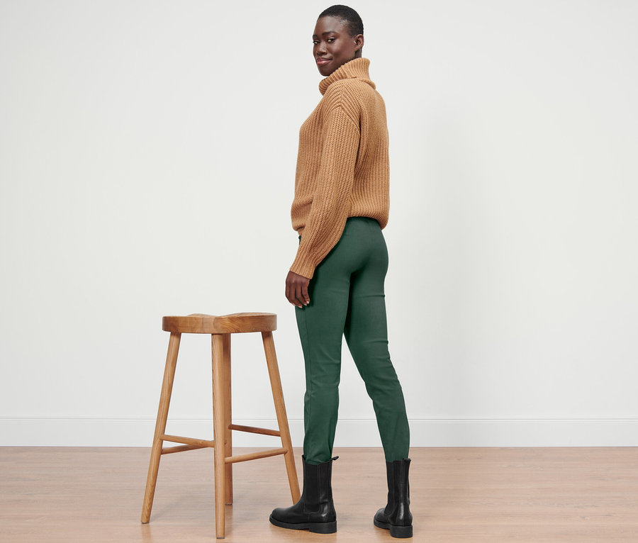 Une femme noire pose de profil face à la caméra, portant un pull et un pantalon stretch vert.