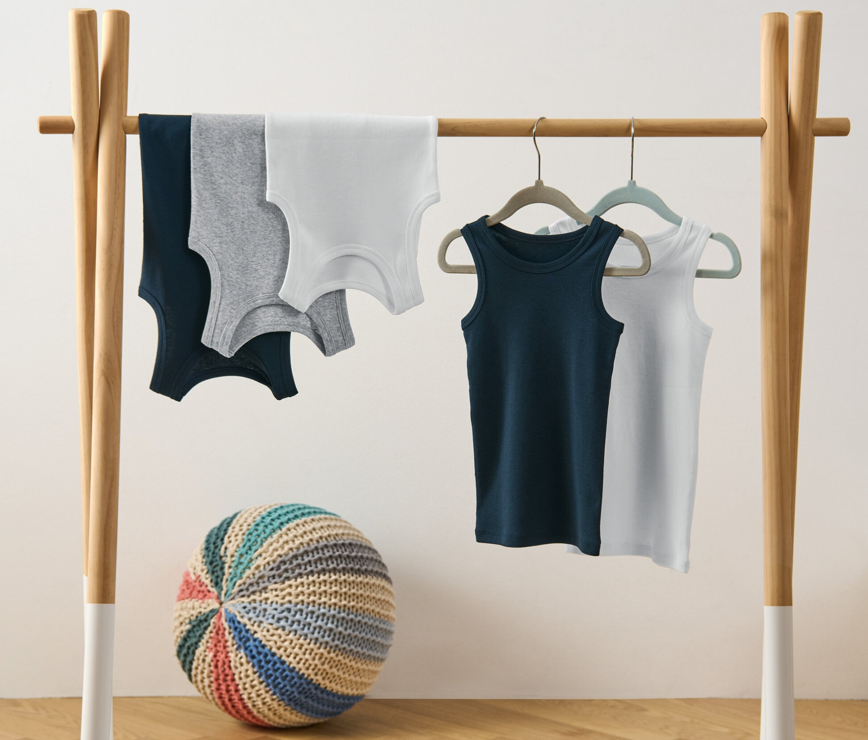 Cinq maillots de corps pour garçon suspendus à un portant.