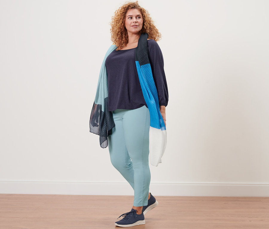 Une femme debout portant une blouse manches 3/4 bleu foncé, une écharpe plissée et un pantalon stretch.