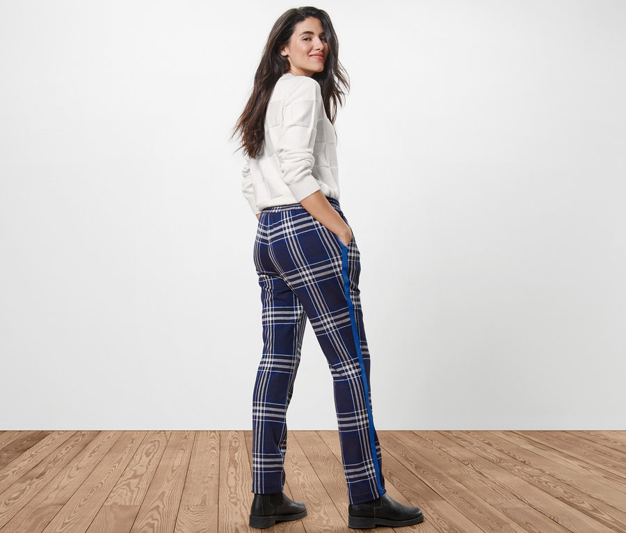 Femme regardant par-dessus son épaule et posant en pantalon de jogging à carreaux, pull et bottes.