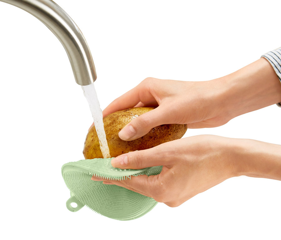 Une personne lave une pomme de terre sous l'eau courante avec 2 éponges de nettoyage en silicone.