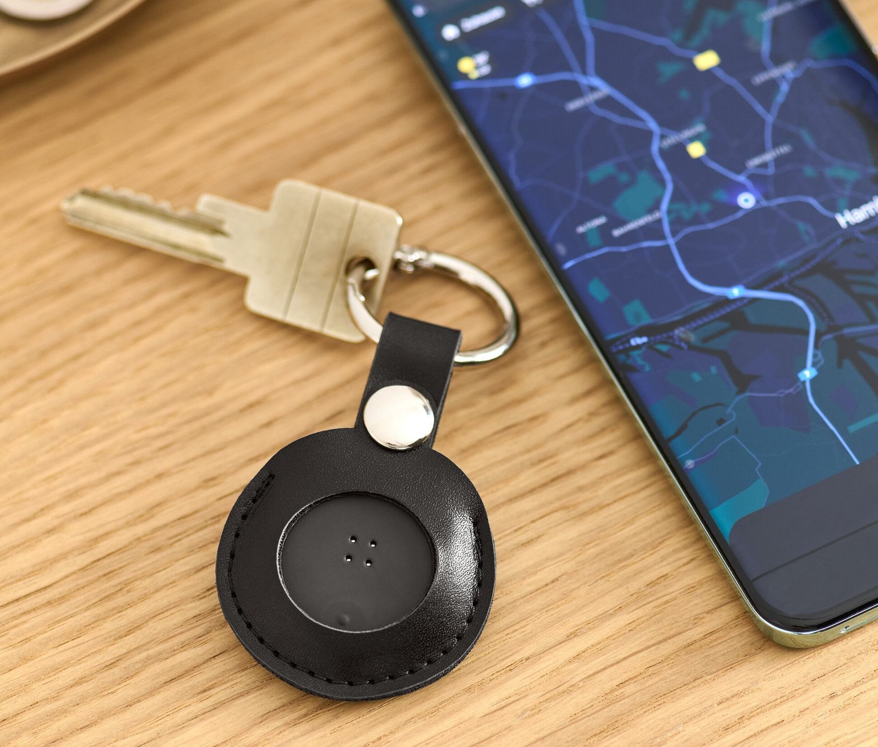Sur une table sont posés des clés avec un tracker intelligent noir avec anneau porte-clé et un téléphone portable affichant une carte.