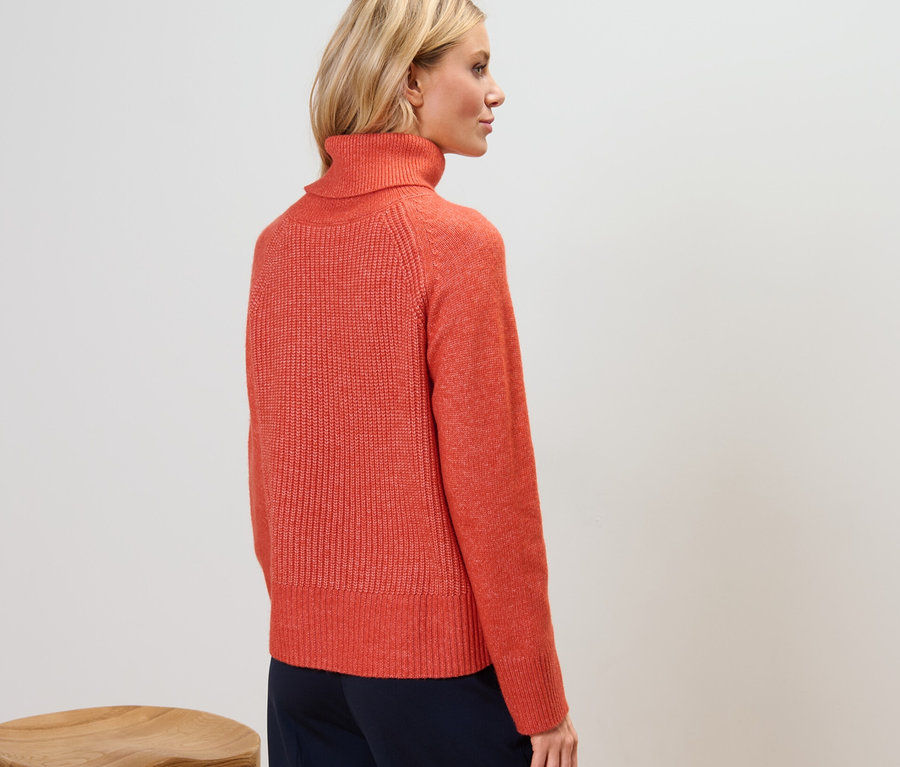 Vue arrière d'une femme portant un pull à col roulé orange en grosse maille.