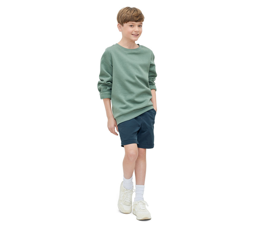 Garçon posant en sweat-shirt vert et short bleu marine. Pantalon fonctionnel pour enfant.