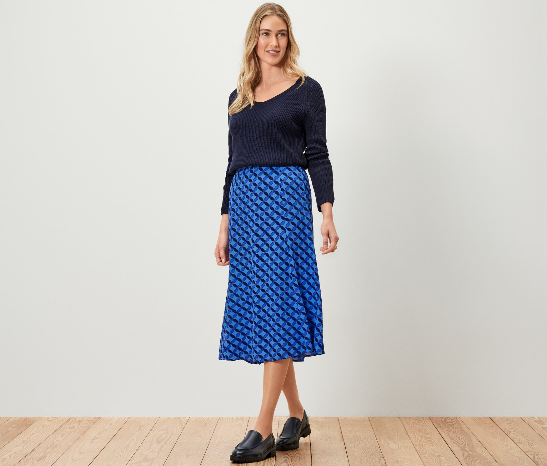 Femme posant en pull bleu marine et jupe midi imprimée bleue.