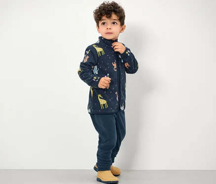 Un garçon porte un pantalon en polaire pour enfant et une veste zippée à motif animalier.
