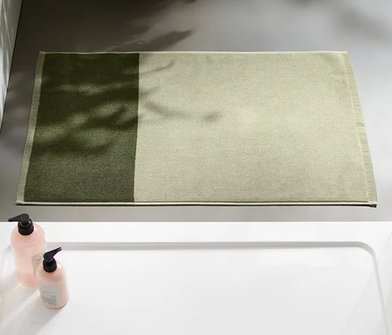 Un tapis de douche jacquard vert sable et vert mousse est posé dans une salle de bain à côté d'une douche.