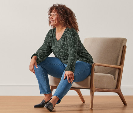 Une femme assise dans un fauteuil porte un chemisier à pois et un jean slim.