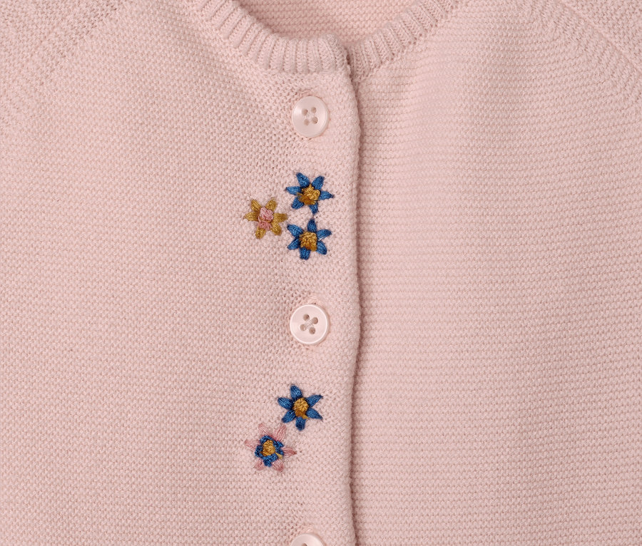 Gros plan sur une combinaison en maille rose pour bébé avec des boutons et des broderies florales.