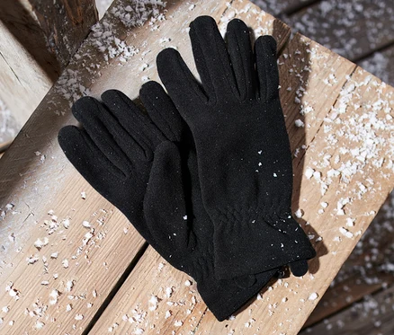 Des gants noirs en micropolaire sont posés sur une surface en bois recouverte de neige.