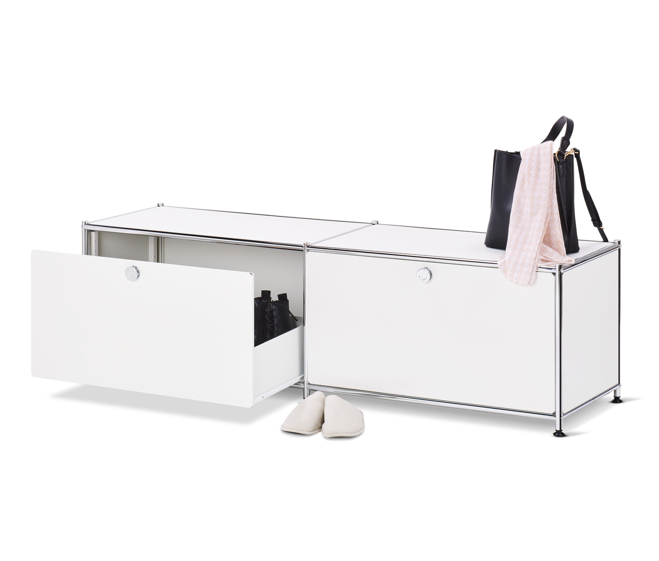 Un meuble bas en métal blanc « CN3 » ouvert avec des tiroirs et des chaussures à l'intérieur, à côté duquel se trouve une paire de chaussons crème, un sac à main noir et une écharpe rose sur le dessus du meuble.