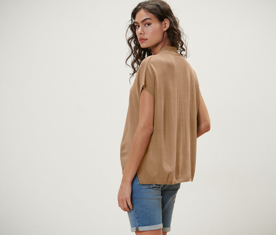 Femme regardant par-dessus son épaule, portant un cardigan beige à manches courtes.