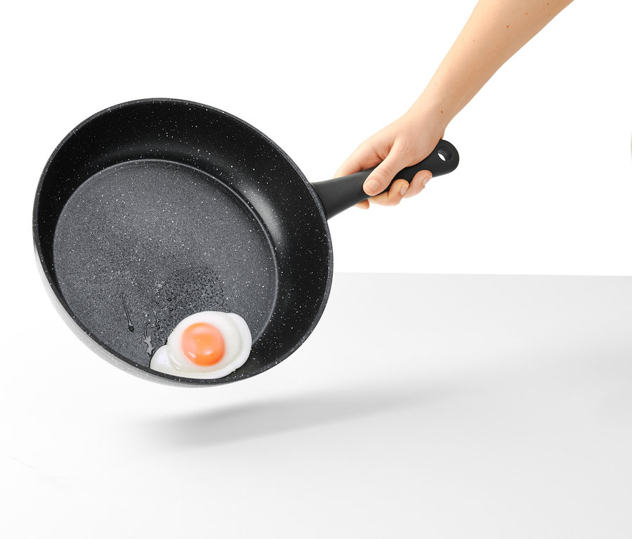 Une main tient une poêle professionnelle de 28 cm à aspect pierre avec un œuf au plat.
