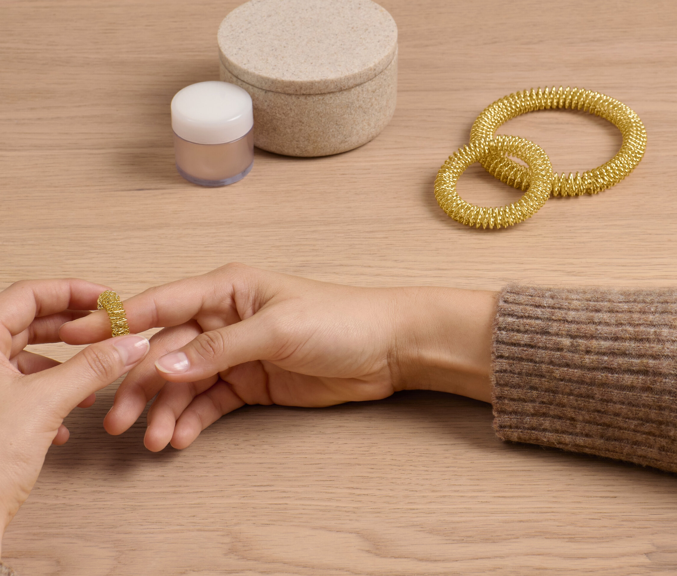 Une femme enfile un anneau d'acupression doré du kit sur son doigt. Deux autres anneaux et une boîte sont posés sur la table.