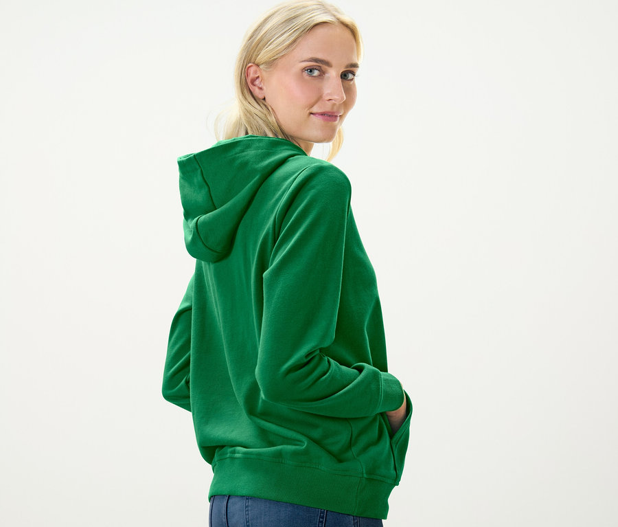 Femme blonde regardant par-dessus son épaule portant un sweat à capuche vert.