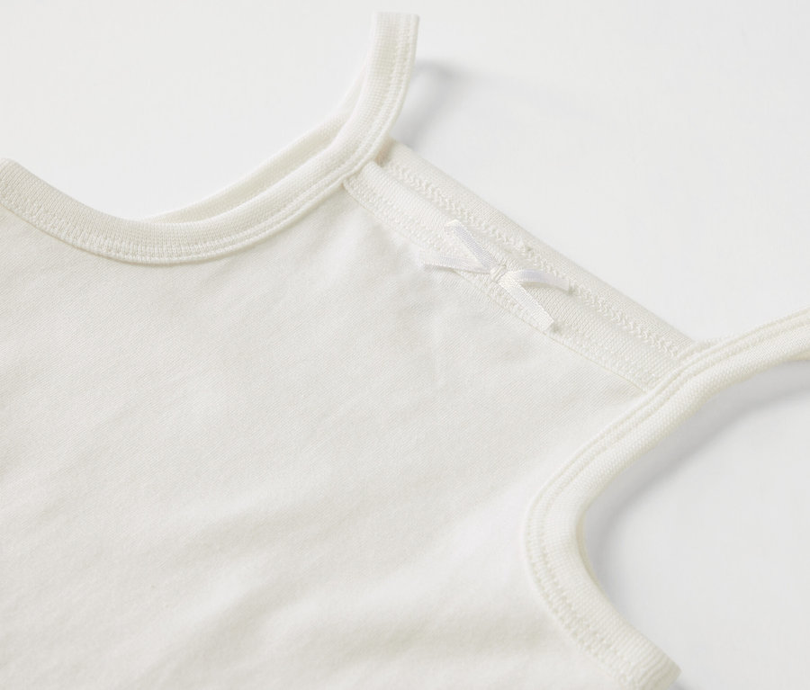 Gros plan sur un body blanc pour bébé avec bretelles et nœud.
