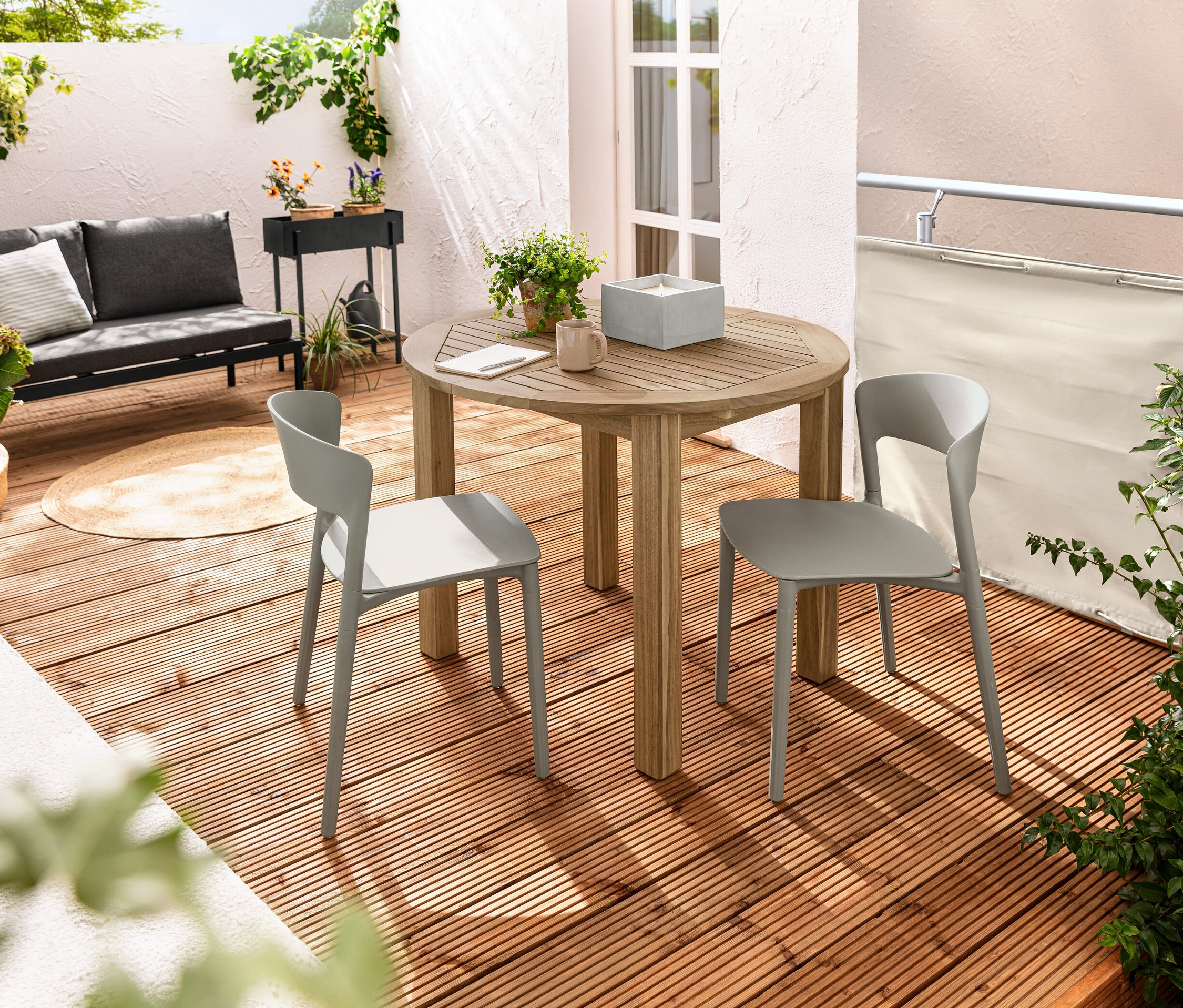 Deux chaises en plastique sont placées près d'une table ronde sur un balcon. Une bougie en cire véritable LED XL est posée sur la table dans un pot en béton. Un brise-vue et brise-vent pour balcon, crème, est visible en arrière-plan.