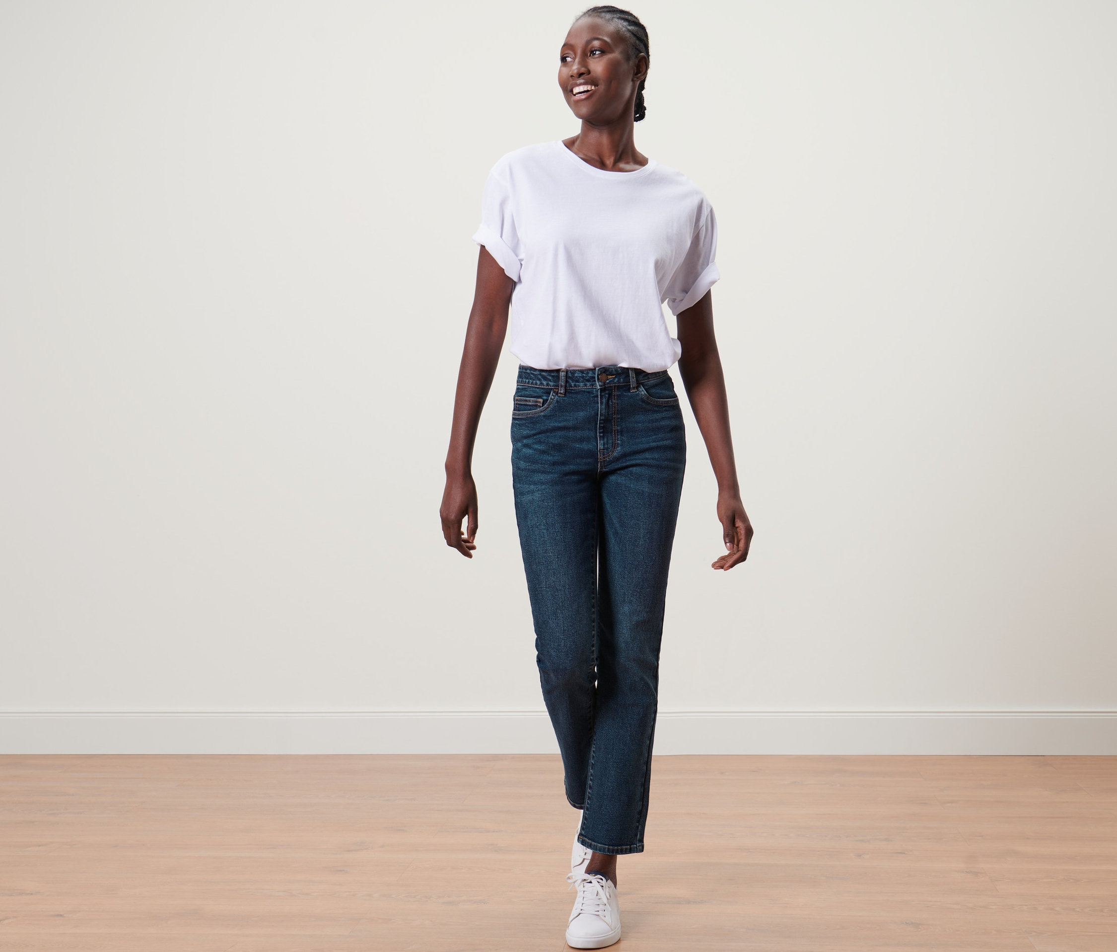Femme marchant et portant un jean droit en denim « Fit Kira », un t-shirt blanc et des baskets blanches.