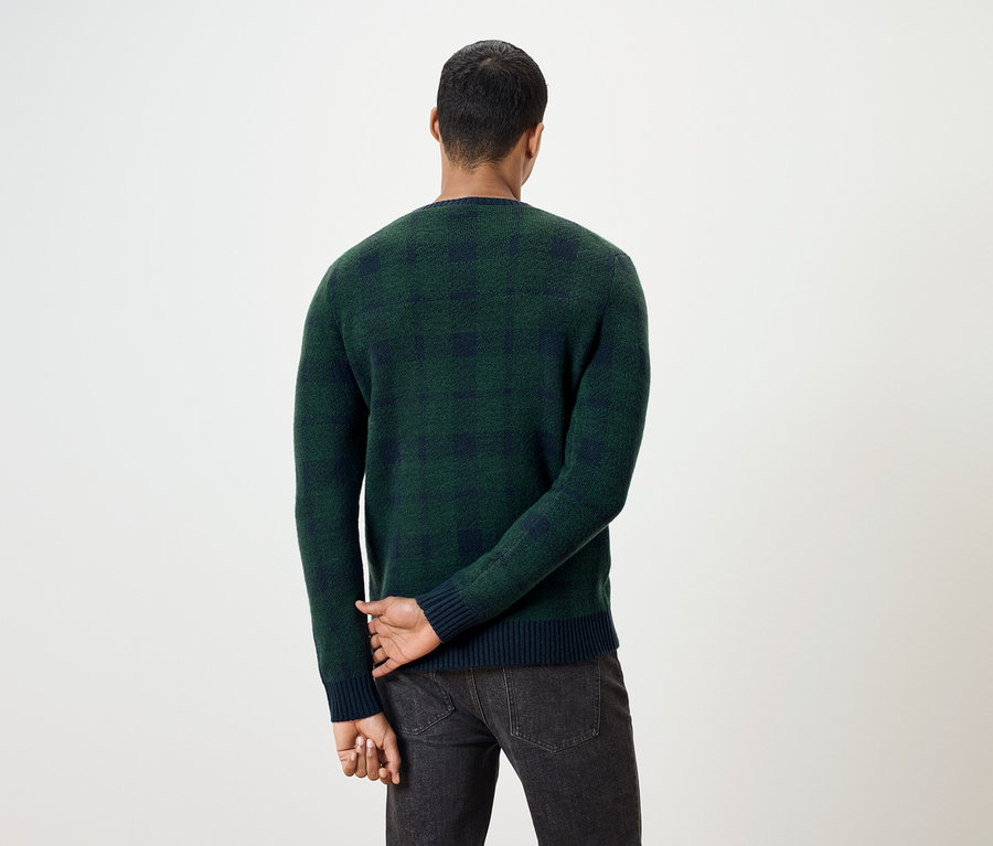 Un homme, dos à la caméra, porte un pull à carreaux vert et un jean foncé.