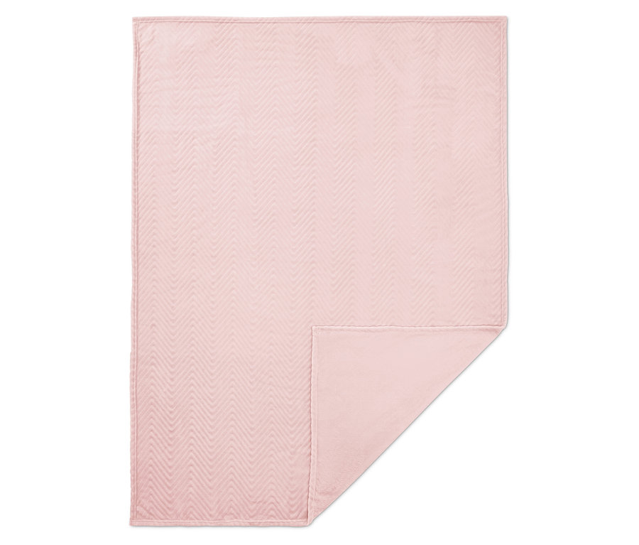 Une couverture rose avec un motif à chevrons matelassé, le coin inférieur est replié.