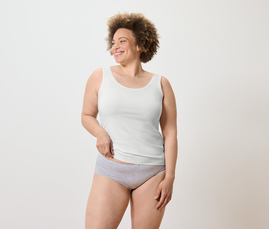 Une femme souriante avec une coupe afro porte un débardeur blanc et une culotte rayée.