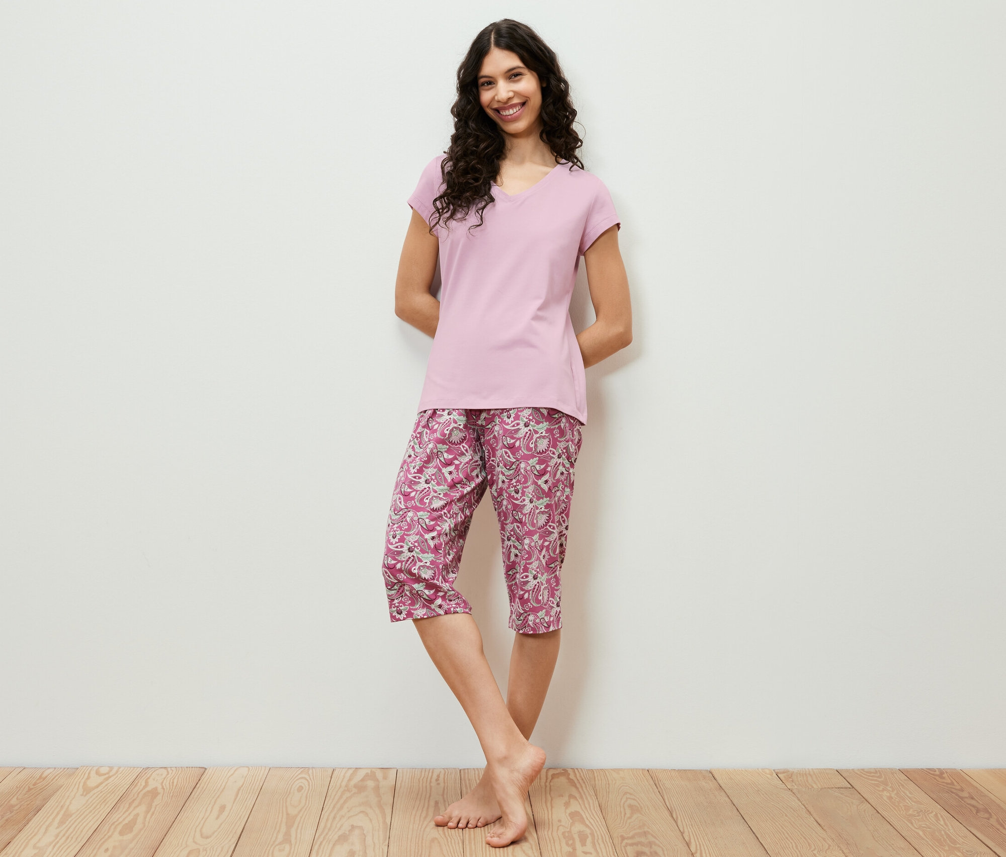 Femme posant sur un plancher en bois dans un ensemble pyjama 3/4 rose.
