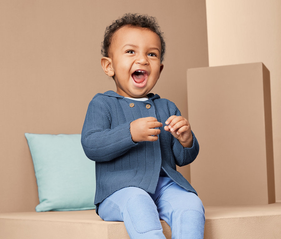 Un enfant est assis et porte une jaquette en maille.
