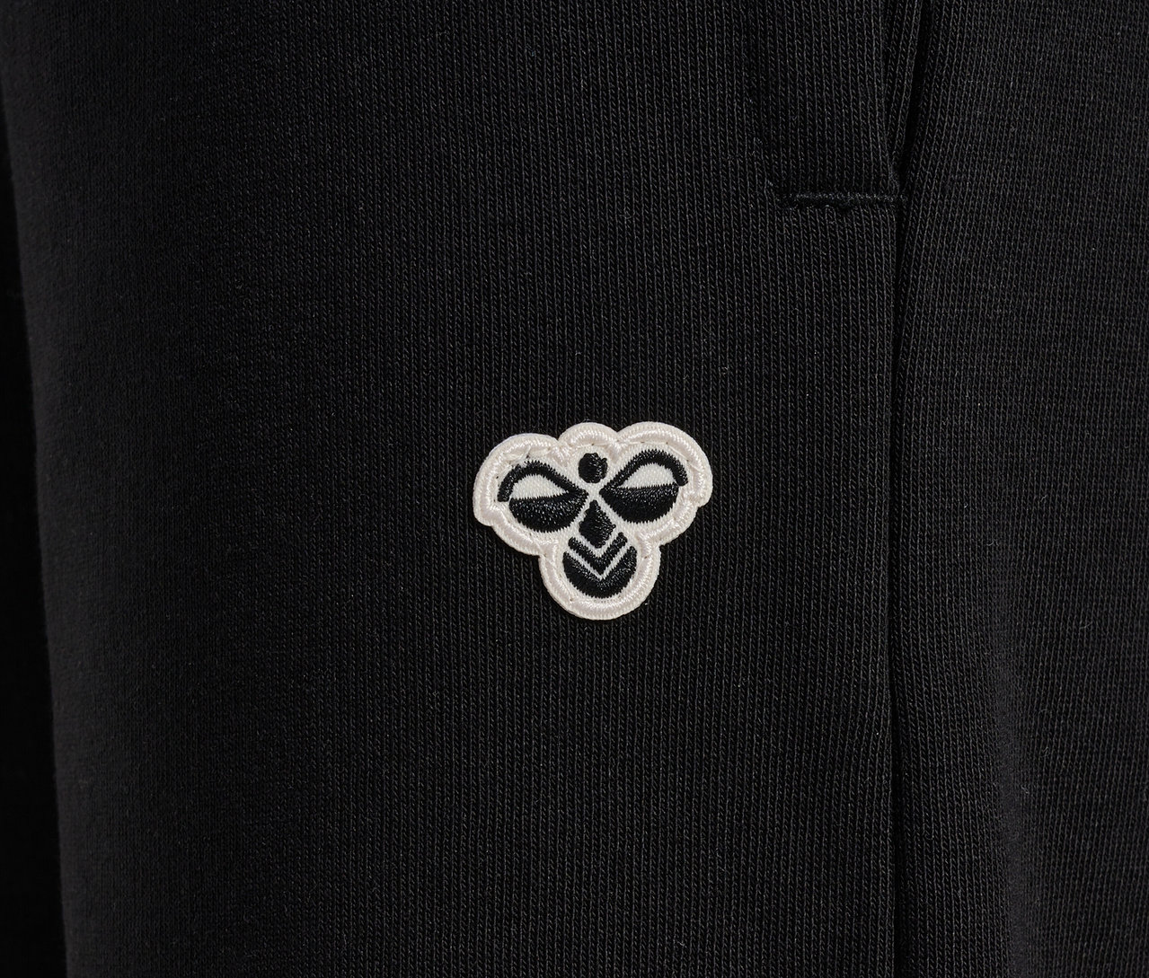 Gros plan d'un pantalon de survêtement noir HUMMEL HMLJR Loose WL avec un logo.