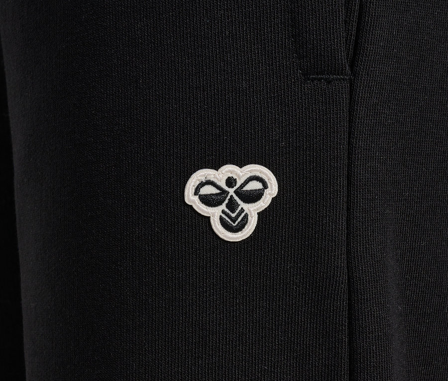 Gros plan d'un pantalon de survêtement noir HUMMEL HMLJR Loose WL avec un logo.