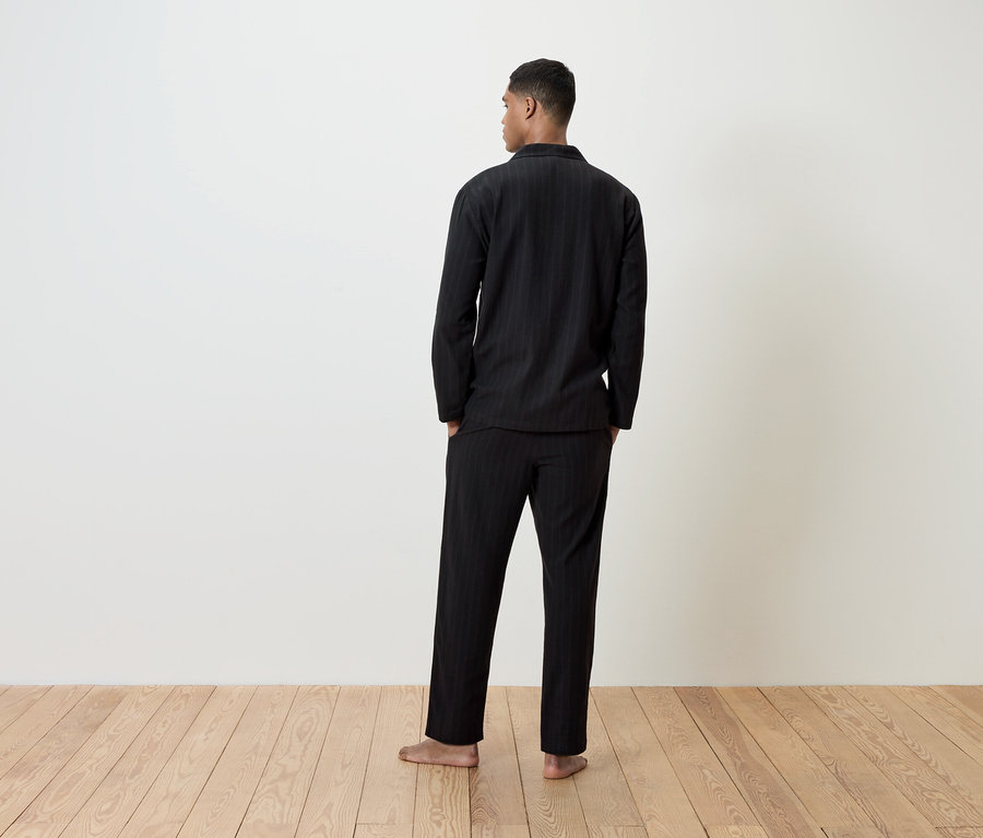 Un homme en pyjama noir se tient dos à la caméra.