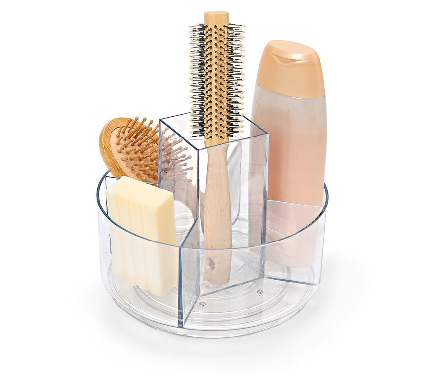 Un récipient transparent rotatif contenant du savon, une brosse à cheveux et un flacon de shampoing.