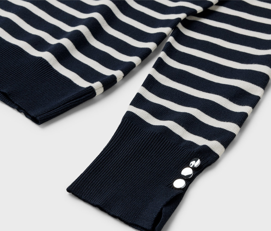 Gros plan sur un pull rayé bleu et blanc à manches longues avec des boutons argentés sur le poignet.