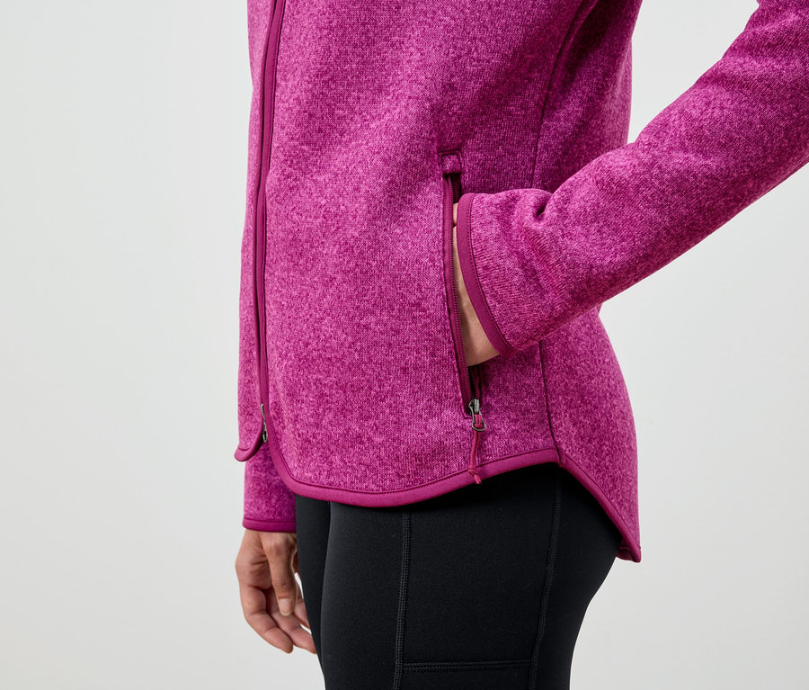 Une femme a sa main dans la poche d'une veste en polaire rose et porte des leggings noirs.