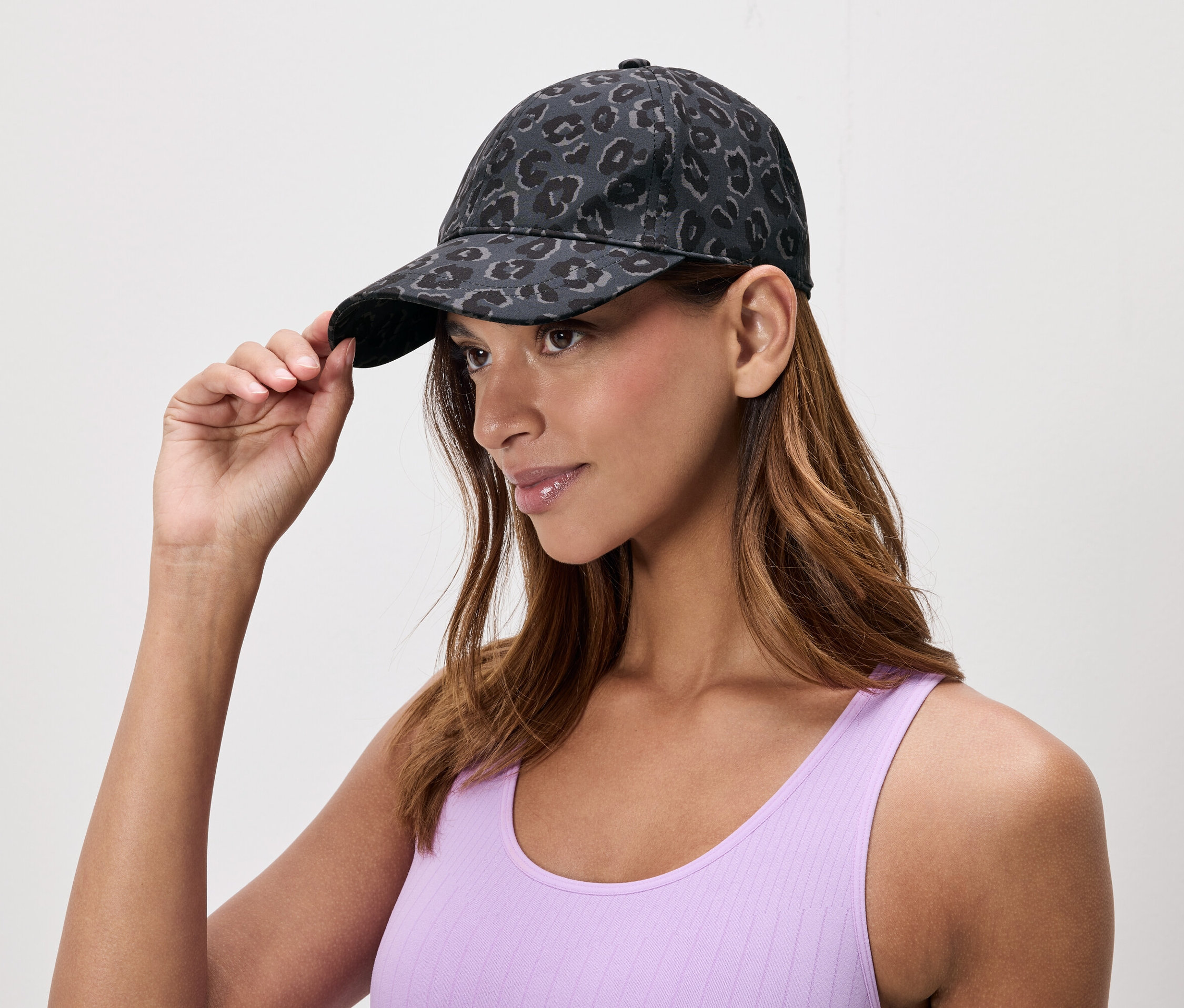 Femme ajustant une casquette à motif animal. Elle porte un débardeur violet.